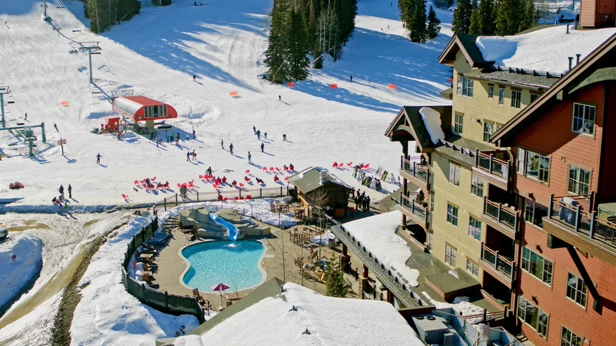 This wide exterior shot captures the ski slopes, pool area, ski lift, and lodge exterior, blending action-packed winter fun with relaxing amenities. It shows the lodge in its full resort context with a lively, cheerful mood.