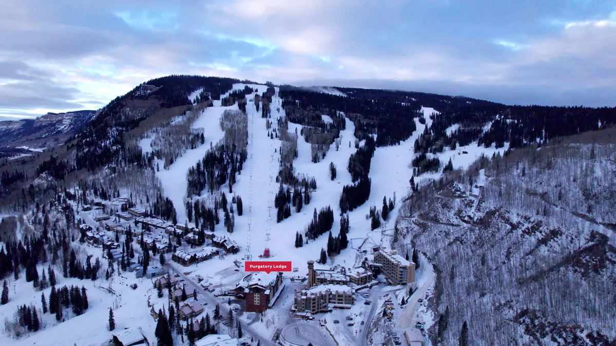 An inviting exterior scene showcasing Purgatory Lodge at sunrise, snow-blanketed ski slopes, and tall pine trees. The area is calm yet brimming with the potential for adventure, with space for family activities like ski lessons or snowball fights.