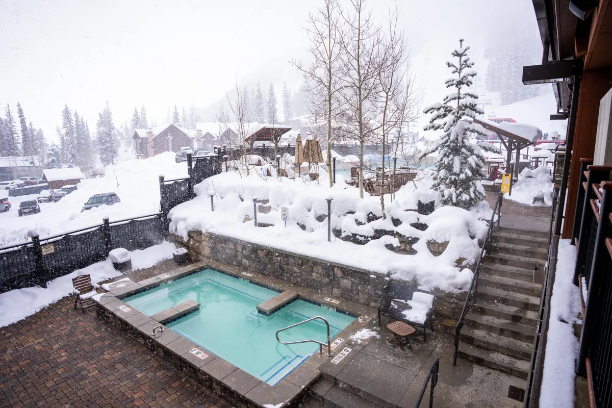 This image features a hot tub set against a snow-covered landscape with trees, suggesting year-round relaxation. People can be seen enjoying the serene atmosphere, reflecting the wellness focus of the section.