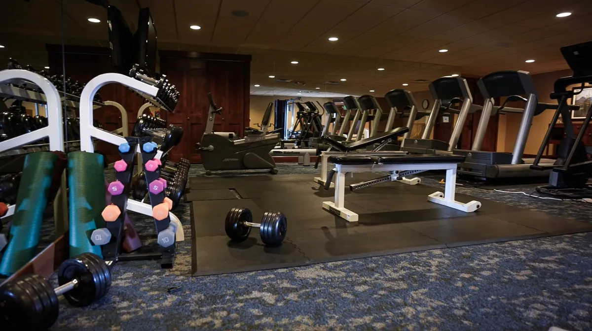 This image features a well-equipped fitness center with dumbbells, a weight bench, treadmills, and exercise mats, all bathed in natural light. The arrangement encourages both individual and group workouts, fostering a sense of community and active living.