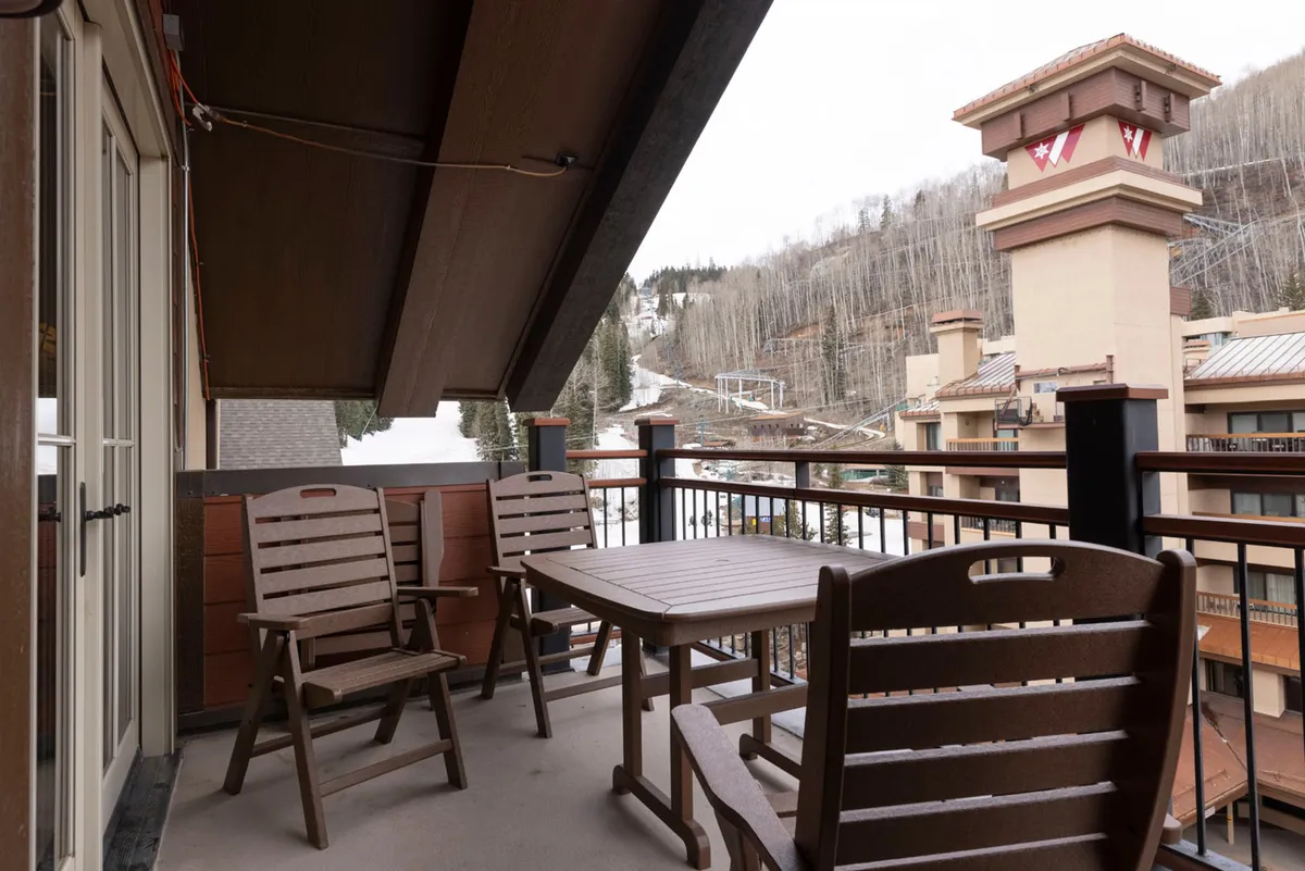 An exterior balcony scene with comfortable outdoor seating, a sturdy wooden railing, and sweeping views of nearby mountains and the village. The setting is perfect for enjoying morning coffee or sharing quiet moments while taking in the panoramic vistas.