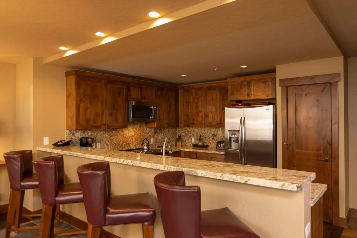 The photo centers on a spacious kitchen island with gleaming granite surfaces, complemented by wood cabinetry and a set of bar stools. The scene suggests sociable cooking sessions or casual breakfasts, with a warm, festive vibe ideal for group meals and celebrations.