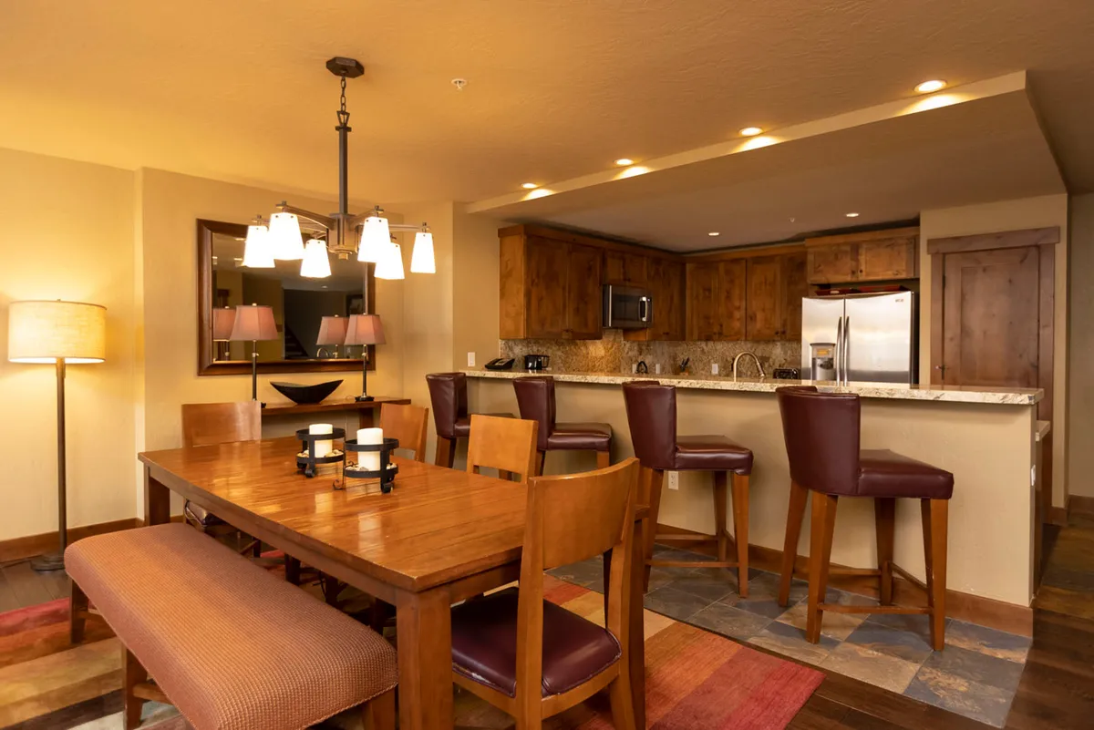A cozy dining area set beside expansive windows, with a large dining table and bar, elegantly lit by modern fixtures. The atmosphere is set for memorable family dinners, intimate celebrations, and lively après-adventure feasts.