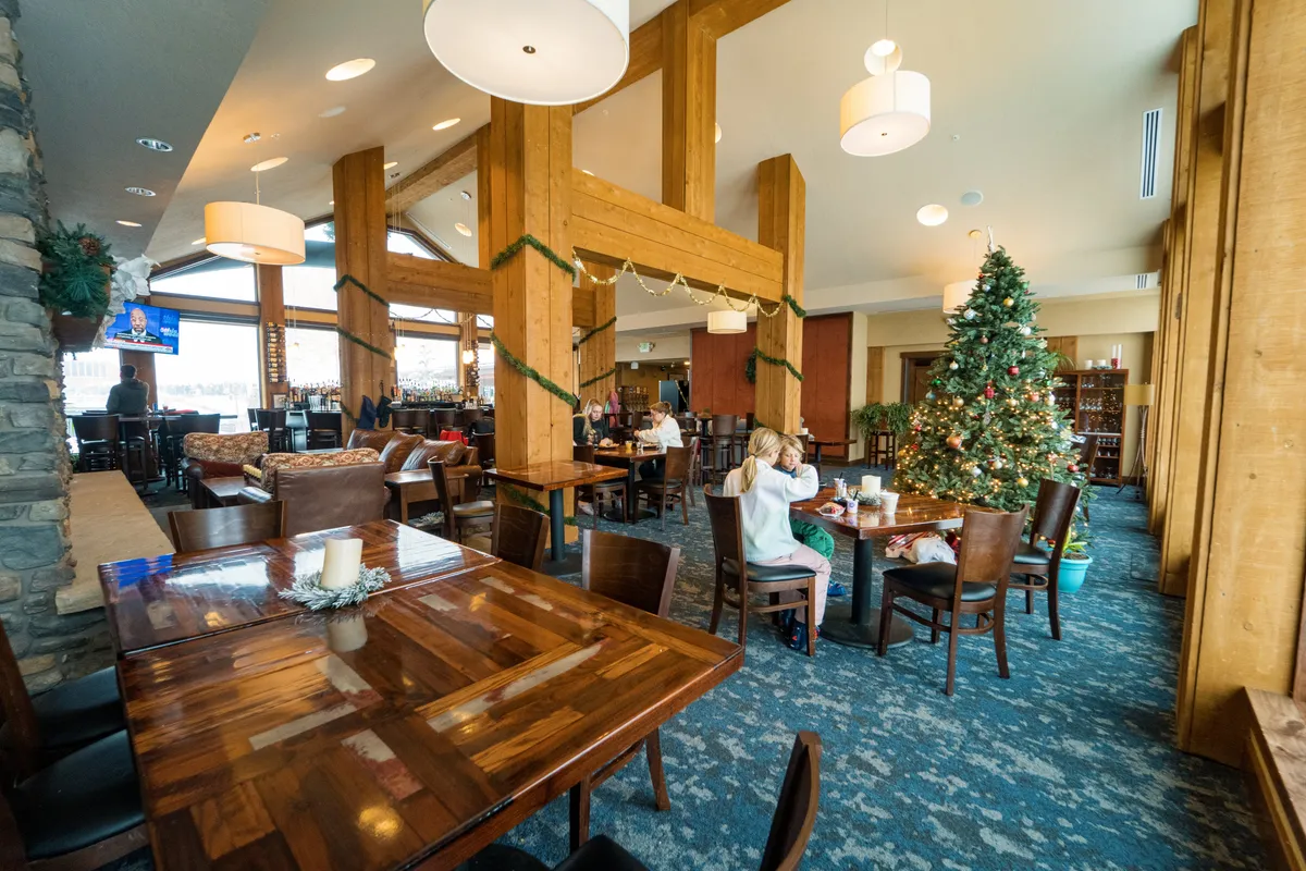 A festive interior dining and social area adorned with a Christmas tree, exposed wooden beams, well-set dining tables, and a welcoming bar area. Warm lighting and holiday decor foster a cozy, communal ambiance perfect for celebrations and shared meals.
